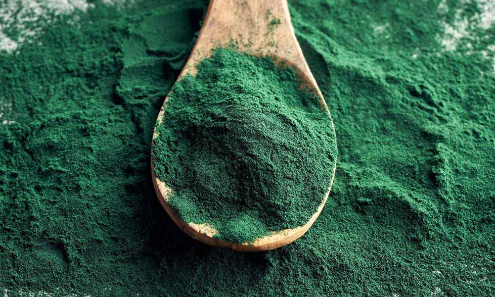 Powdered spirulina on a wooden spoon spilling onto a table